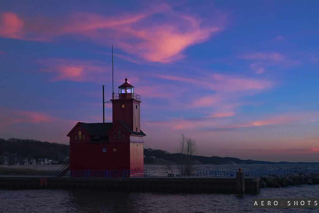 a red building on a dock with Holland Harbor Light in the background